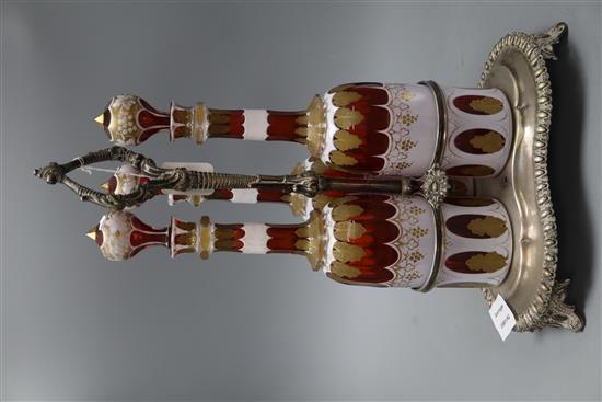 A plated three bottle tantalus, the decanters overlaid glass with gilt decoration, height 37cm
